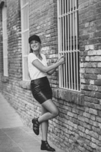 Young blonde woman wearing cap smiling near a brick wall