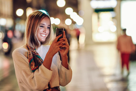 Woman taking photograph with smartphone at night in the street