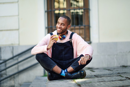 Young black man eating an apple sitting on urban steps