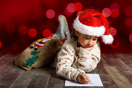 Adorable little girl wearing santa hat writing Santa letter