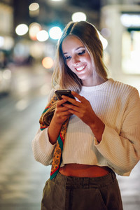 Woman with defocused urban city lights looking at her smartphone