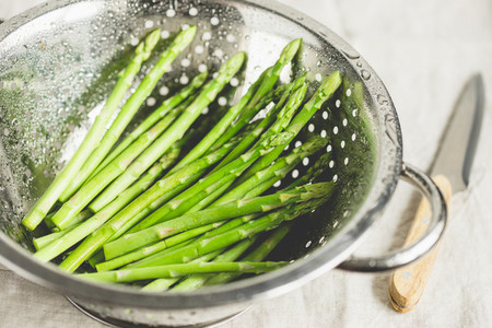 Washed asparagus in a metal colander on a kitchen table  Preparation vegetarian healthy food
