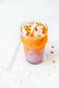 Orange and purple vegan smoothie is made from blueberry  sea buckthorn  coconut cream  nuts and chia on a white background  The concept of healthy summer food and drink