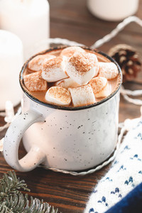 Hot chocolate with marshmallow in a white ceramic mug among winter things and decor on a wooden table  The concept of cosy holidays and New Year