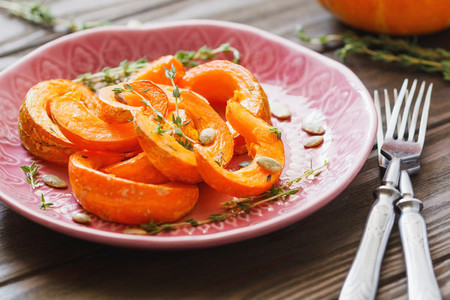 Baked pumpkin slices with thyme on a wooden board over grey table  Seasonal food vegetarian recipe