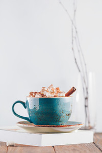 Hot chocolate with marshmallows and cinnamon stick in a blue ceramic cup on a table with a book  The concept of winter or fall time  Minimal scandinavian design