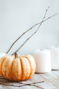 Small pumpkin and white candles still life near white wall Autumn background