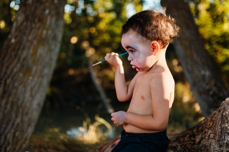 Kid painting himself of dracula to halloween on the forest