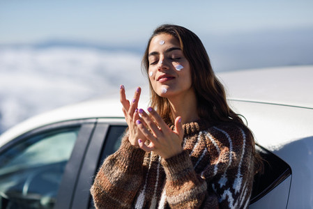 Young woman applying sunscreen on her face in snow landscape