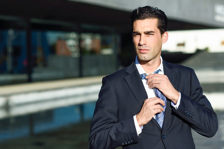 Young handsome businessman adjusting a tie in urban background
