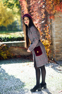 Young beautiful girl wearing winter coat and cap in autumn leaves background