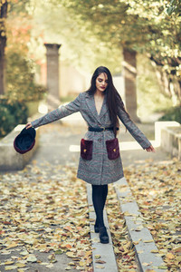 Young girl with very long hair wearing winter coat and cap in urban park full of autumn leaves