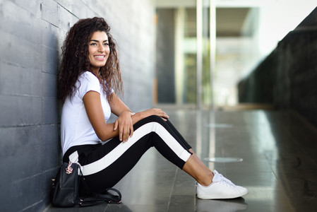 Happy African woman with black curly hairstyle sitting on urban