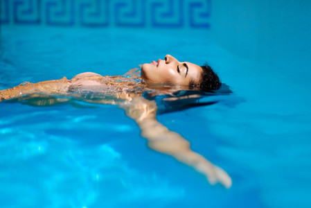 Beautiful tanned woman in bikini relaxing in swimming pool