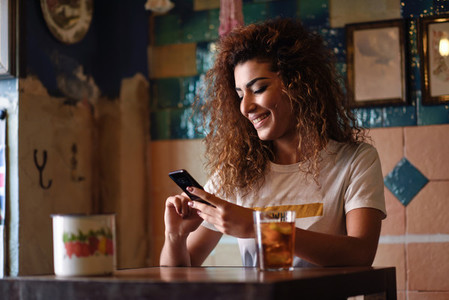 Arabic smiling woman in a beautiful bar looking at her smartphon