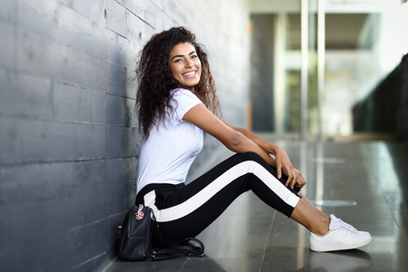 Happy African woman with black curly hairstyle sitting on urban floor