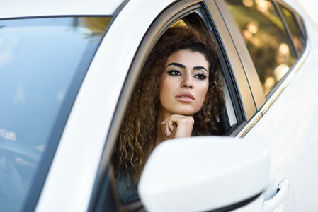 Young arabic woman inside a white car looking through the window