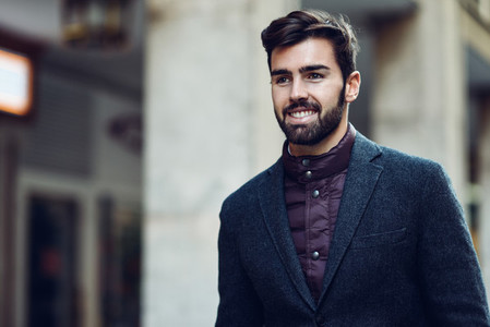 Young bearded smiling man wearing british elegant suit in the st