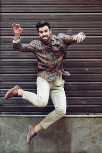 Young bearded man jumping in urban background with open arms wea