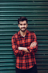 Young bearded smiling man wearing a plaid shirt with a green bli