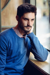 Pensive man with blue sweater with lost look near a window