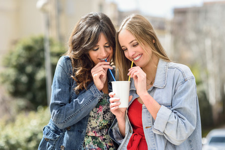 Two young women drinking the same drink with two straws