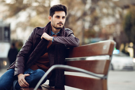 Thoughtful young man sitting on an urban bench
