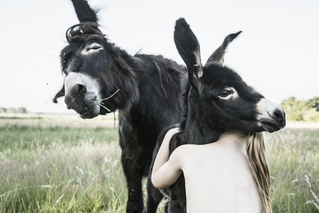 Bare chested girl hugging baby donkey in rural field