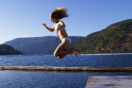 Carefree girl jumping off dock into sunny lake  Lake Cowichan  British Columbia  Canada