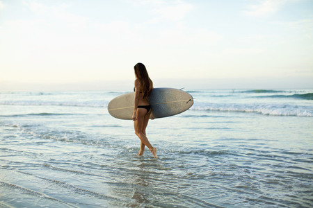 Female surfer carrying surfboard in ocean surf