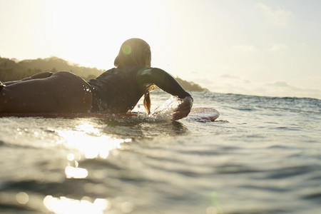 Female surfer paddling out on sunny sunset ocean