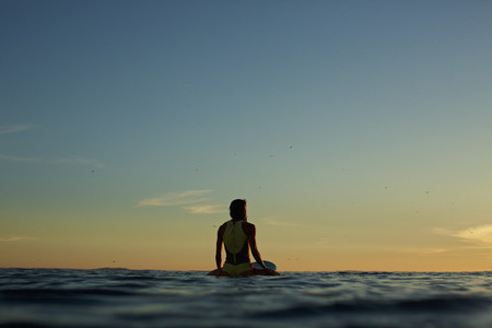 Female surfer waiting on surfboard on ocean at sunset