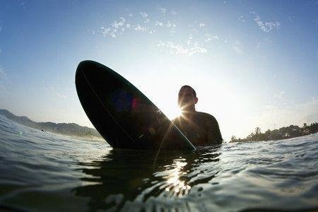 Silhouette male surfer straddling surfboard in sunny ocean