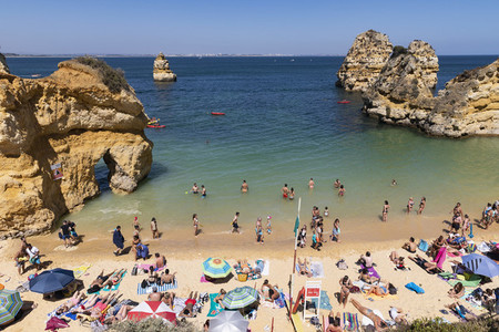 Tourists sunbathing and swimming on sunny summer beach Lagos Algarve Portugal