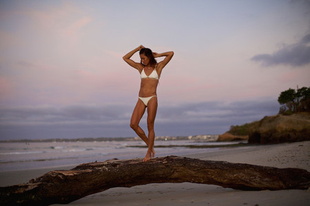 Woman in bikini walking on driftwood on beach at dusk