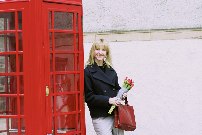 Woman with bunch of tulips leaning against red telephone box
