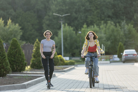 Women friends riding bicycle and push scooter on road