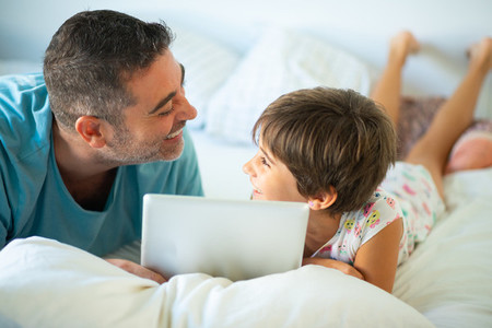 Middle age father with her eight years daughter using digital tablet in bedroom