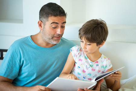Middle age father with her eight years daughter using digital tablet in bedroom