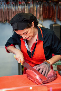 Woman cutting fresh meat in a butcher shop with metal safety mesh glove