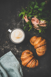 Cup of cappuccino fresh croissants and flowers over shabby background