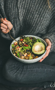 Woman sitting and eating healthy vegetarian dinner from Buddha bowl