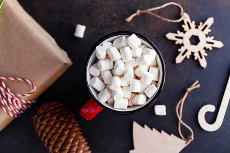Hot chocolate in a red mug with marshmallow surrounded Christmas decoration