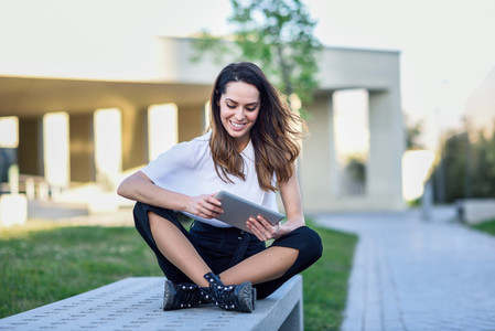 Middle age woman using digital tablet sitting outdoors in urban background