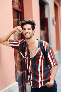Smiling young man with dark hair and modern hairstyle wearing casual clothes outdoors