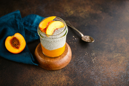 Portion healthy vegan chia pudding with almond milk  vanilla and peaches in a glass jar on a dark table