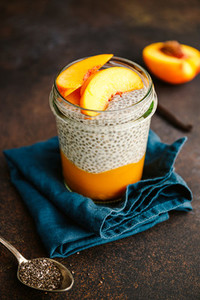 Portion healthy vegan chia pudding with almond milk  vanilla and peaches in a glass jar on a dark table