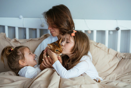 Happy mother and two daughters smiling hugs in bed