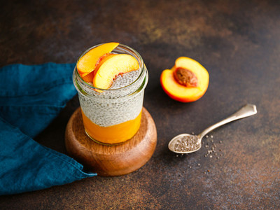 Portion healthy vegan chia pudding with almond milk vanilla and peaches in a glass jar on a dark table