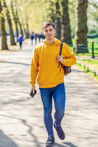 Young urban man using smartphone walking in street in an urban park in London